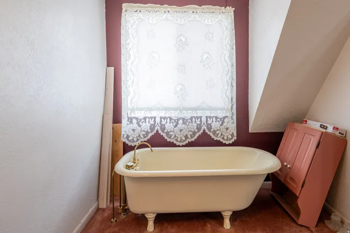 White clawfoot bathtub featuring brass fixtures and a decorative lace window covering