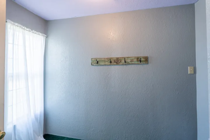Light gray wall with textured finish, featuring a rustic wooden coat rack with four hooks