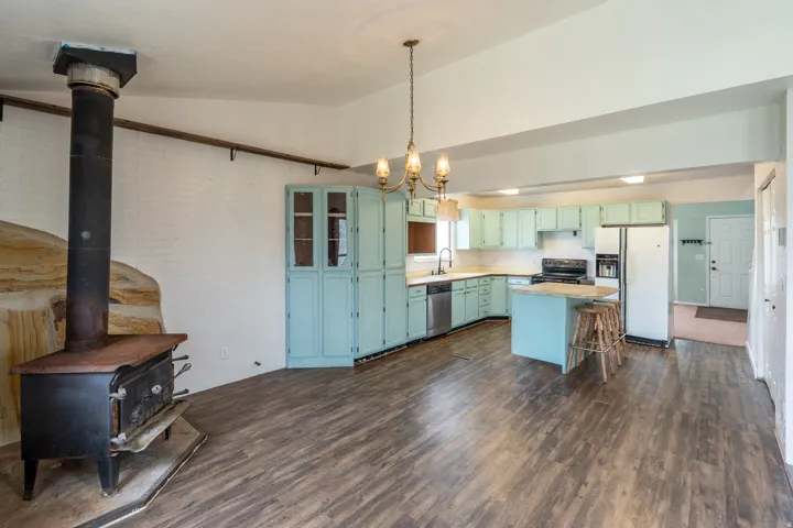 Spacious open concept room featuring wood-finish flooring, a built-in wood-burning stove with a stone surround, and a kitchen with light blue cabinetry, a central island, and white appliances