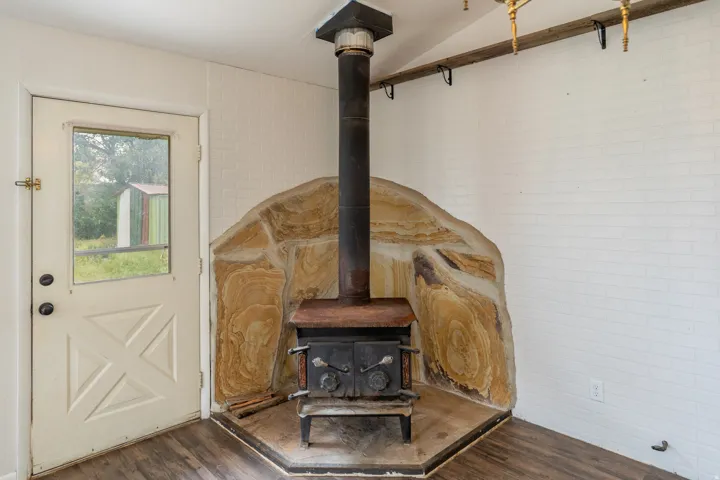 Wood-burning stove with a stone surround, wood-finish flooring, and white painted brick accent wall