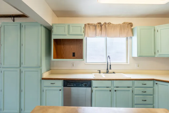 Kitchen featuring light blue cabinetry, dual-basin sink with gooseneck faucet, stainless steel dishwasher, and a window above the sink