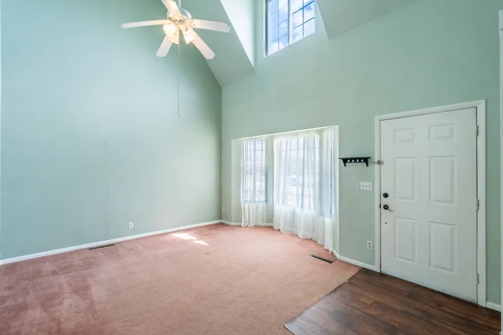 Vaulted ceiling with ceiling fan, upper transom windows, bay windows with sheer curtains, wood-finish flooring at entry, and paneled entry door