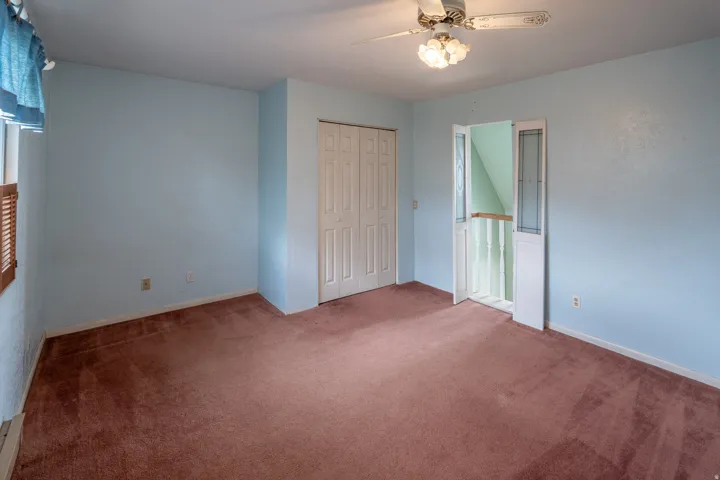 Carpeted room with a ceiling fan light fixture, bifold closet doors, and wood window blinds