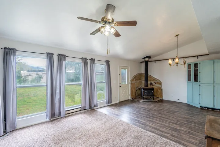 Bright living area featuring multiple large windows, a stone-surrounded wood-burning stove, wood-finish flooring, and a ceiling fan
