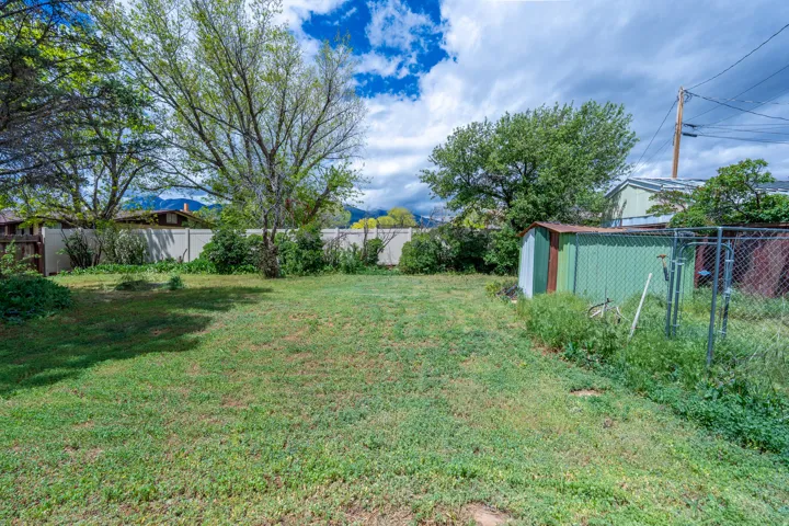Expansive outdoor space featuring a large grassy area, mature trees, a privacy fence, and a utility shed