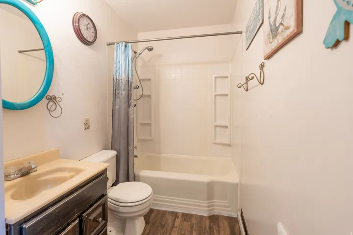 Bathroom featuring wood-finish flooring, a white integrated tub and shower unit, and a vanity with a dark cabinet and integrated sink