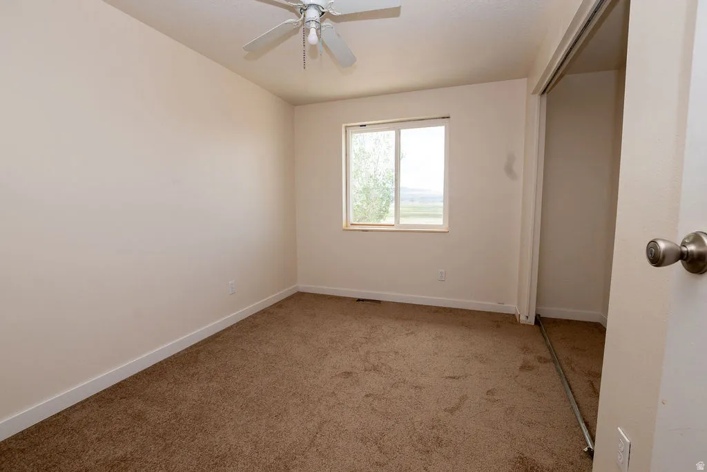Carpeted interior space featuring a ceiling fan with light fixture, a window offering exterior views, and a closet with sliding doors