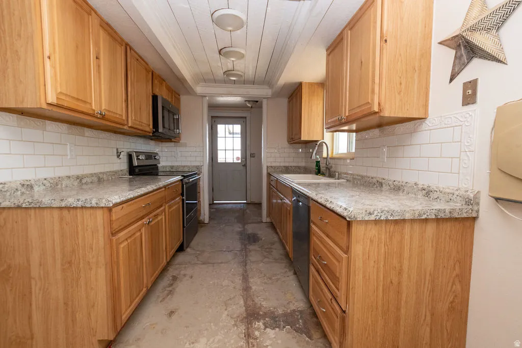 Galley-style kitchen featuring light wood cabinetry, stone-look countertops, and white subway tile backsplash