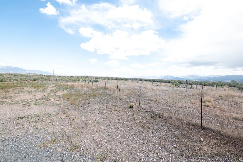 Expansive undeveloped land featuring a wire fence, natural vegetation, distant mountains, and an open sky