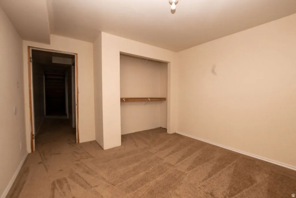 Carpeted room featuring a built-in closet with shelving and hanging rods, neutral wall color, and white baseboards