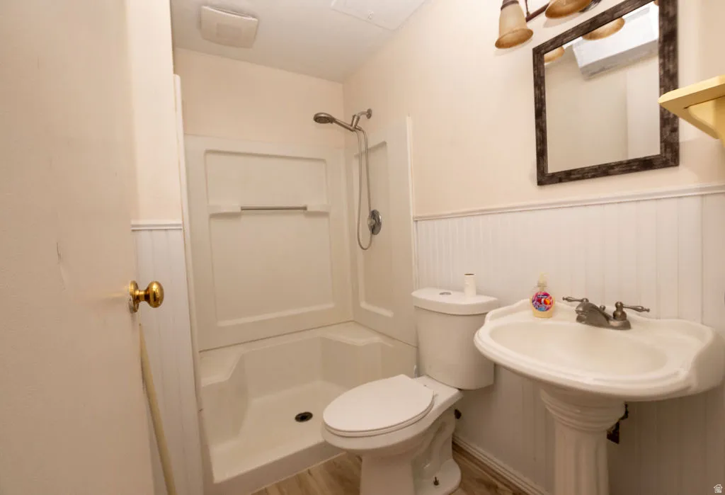 Bathroom featuring a pedestal sink, toilet, and white fiberglass shower stall with a showerhead