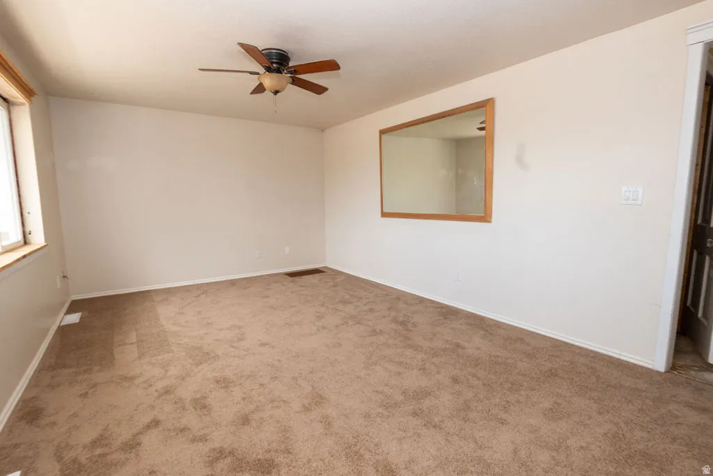 Room featuring neutral carpeting, light-toned walls, and a ceiling fan with wood-finish blades