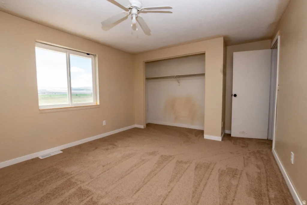 Light brown carpet flooring with white baseboards, a window with exterior visibility, a built-in closet, and a ceiling fan