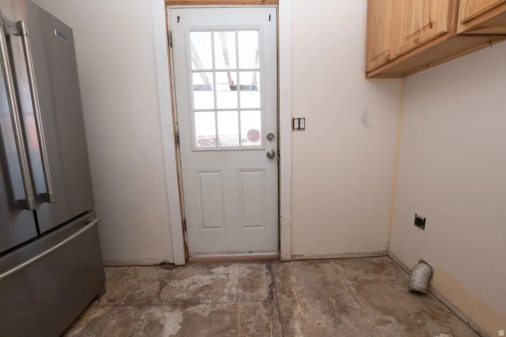 Utility space featuring a partial stainless steel refrigerator, light-toned upper cabinetry, and a door with divided lites