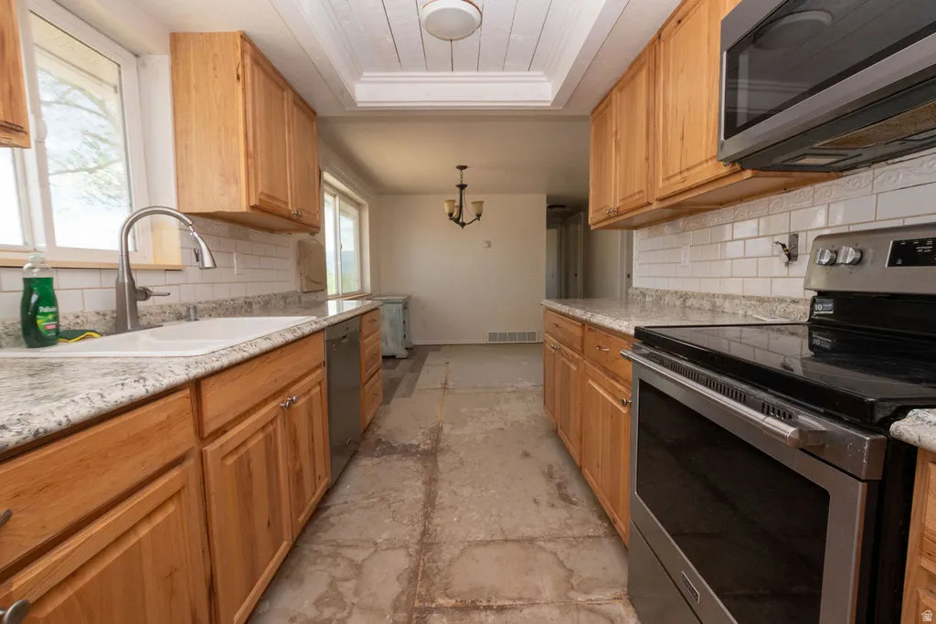 Kitchen featuring light wood cabinetry, white subway tile backsplash, granite-finish countertops, stainless steel appliances, and a recessed ceiling with wood paneling