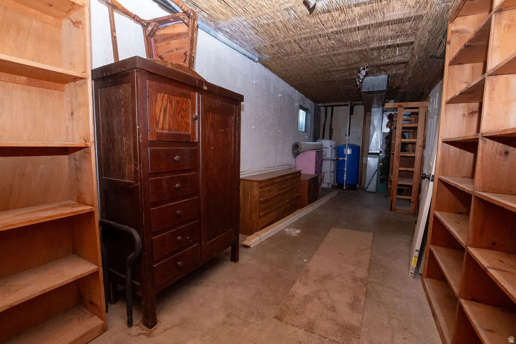 Unfinished room featuring concrete flooring, exposed ceiling with woven material, light wood shelving, and a small window