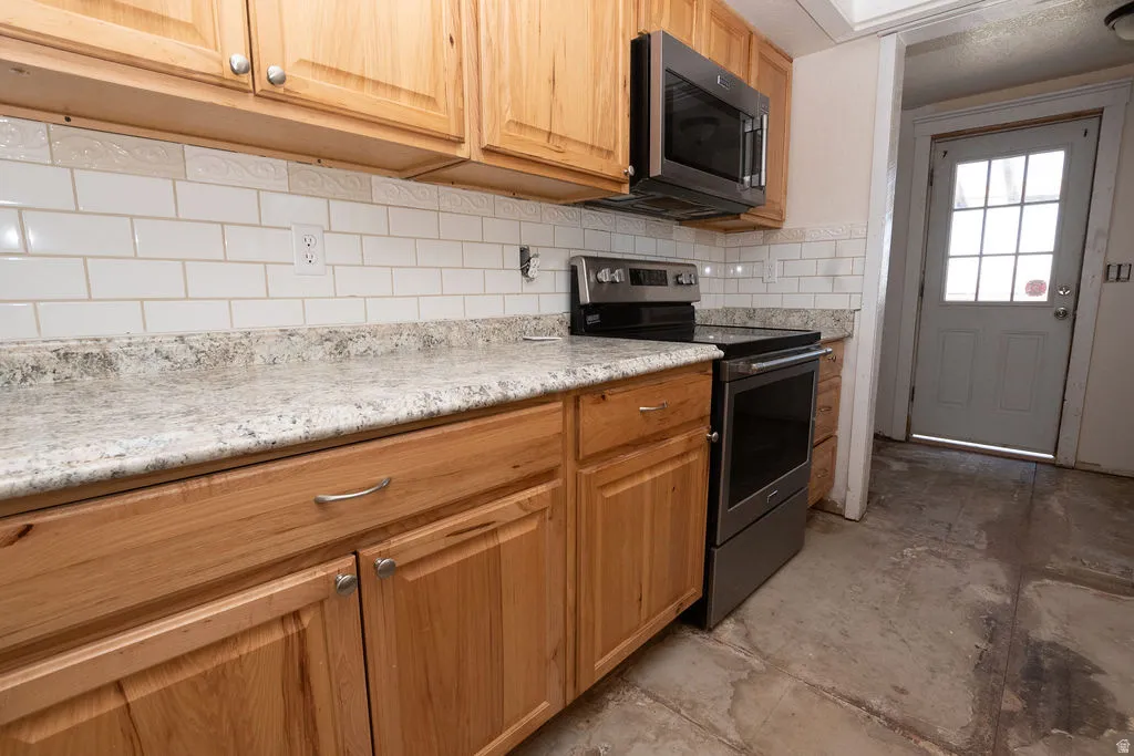 Kitchen featuring light wood cabinetry, stone-finish countertops, and a subway tile backsplash