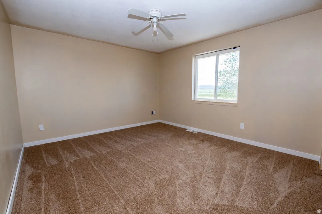 Carpeted room featuring a ceiling fan, beige walls, and a window with white trim