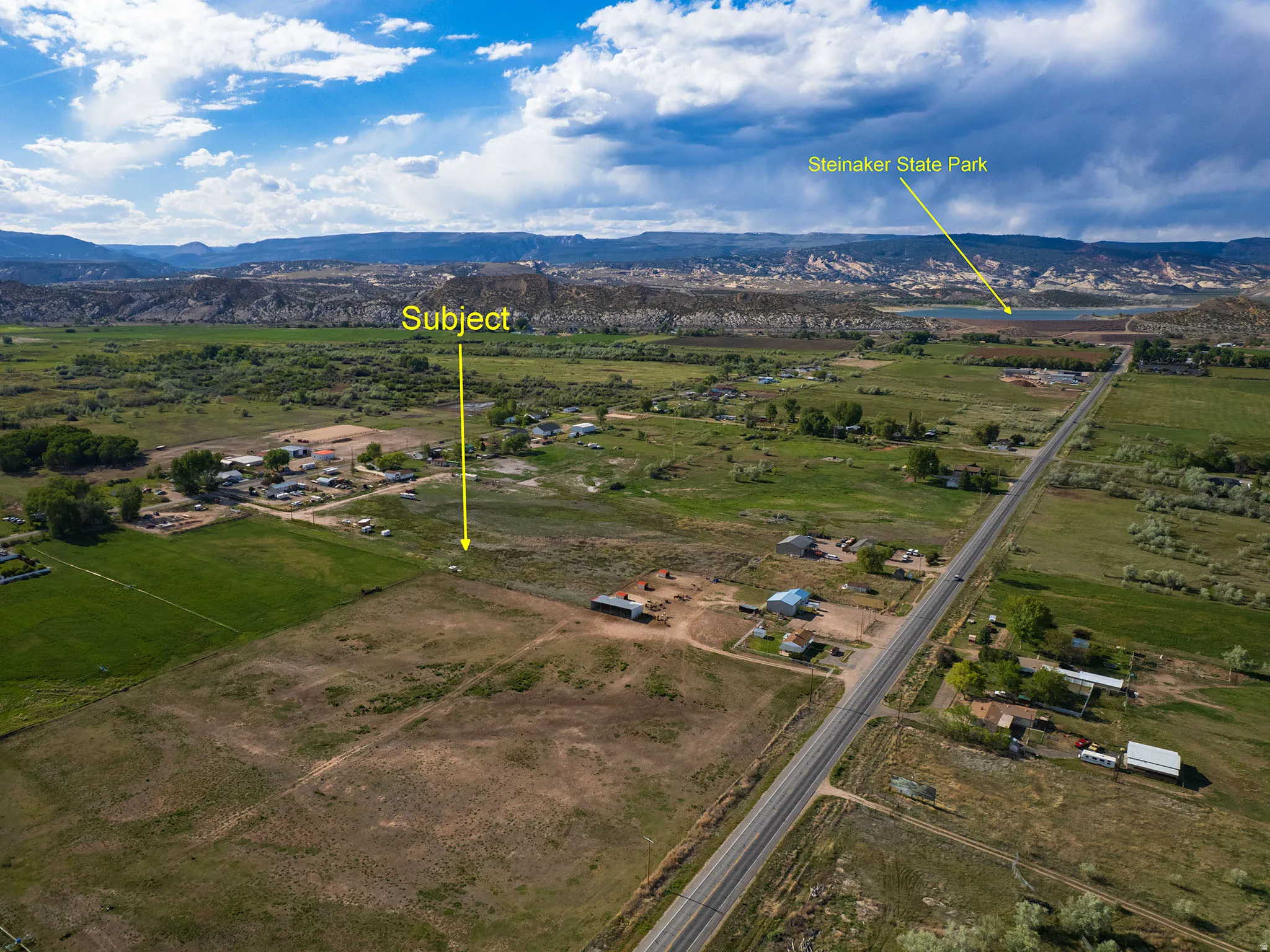 Expansive undeveloped land featuring a cleared building site, direct road frontage, and a distant mountainous backdrop