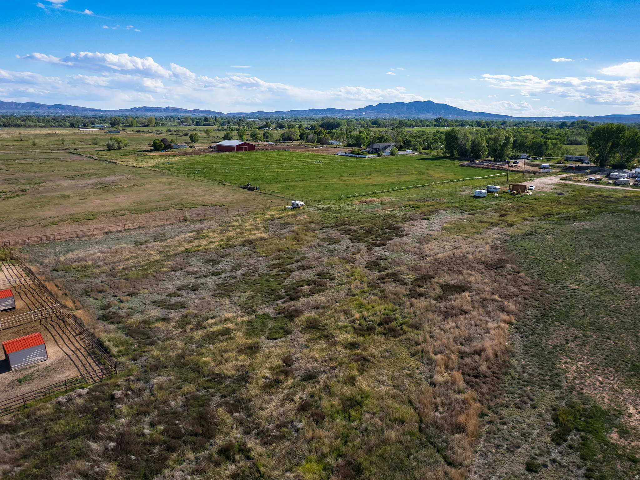 Expansive property featuring a red barn, multiple outbuildings, fenced areas, and surrounding green fields