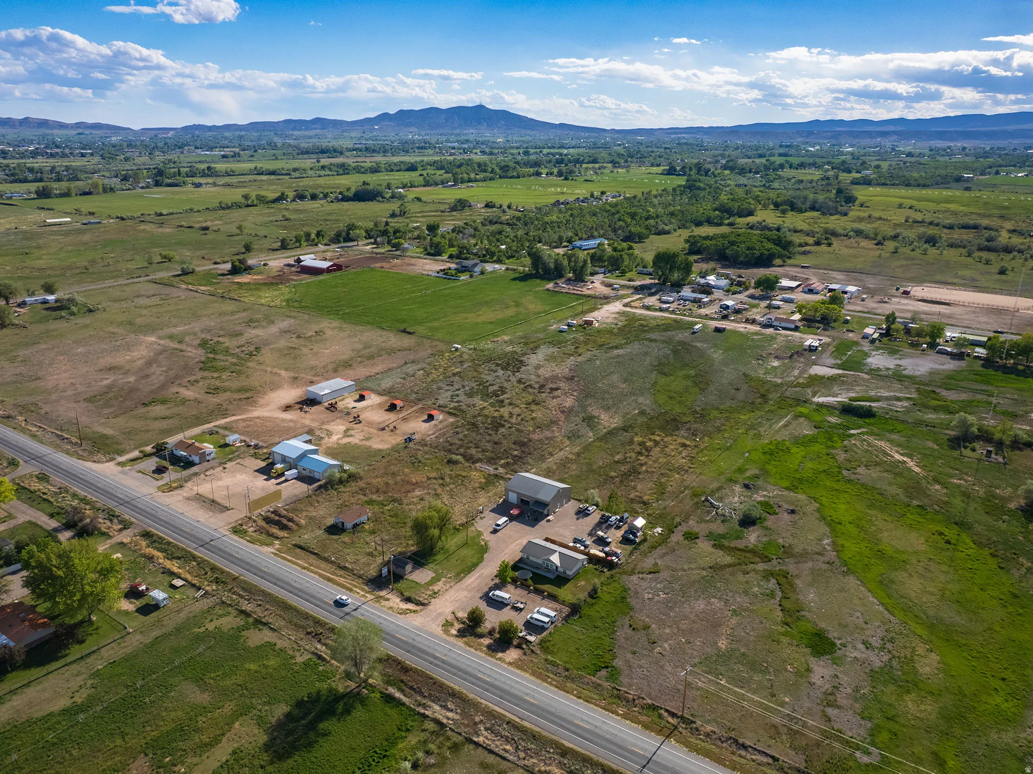 Expansive acreage featuring a paved road frontage, multiple existing structures, varied terrain, and distant mountain backdrops