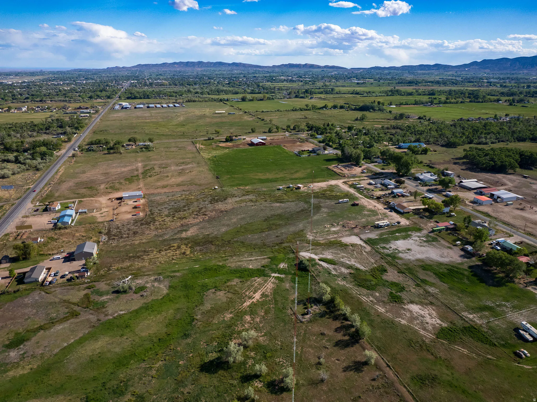Expansive rural landscape featuring scattered residential and agricultural structures, open fields, and distant mountains