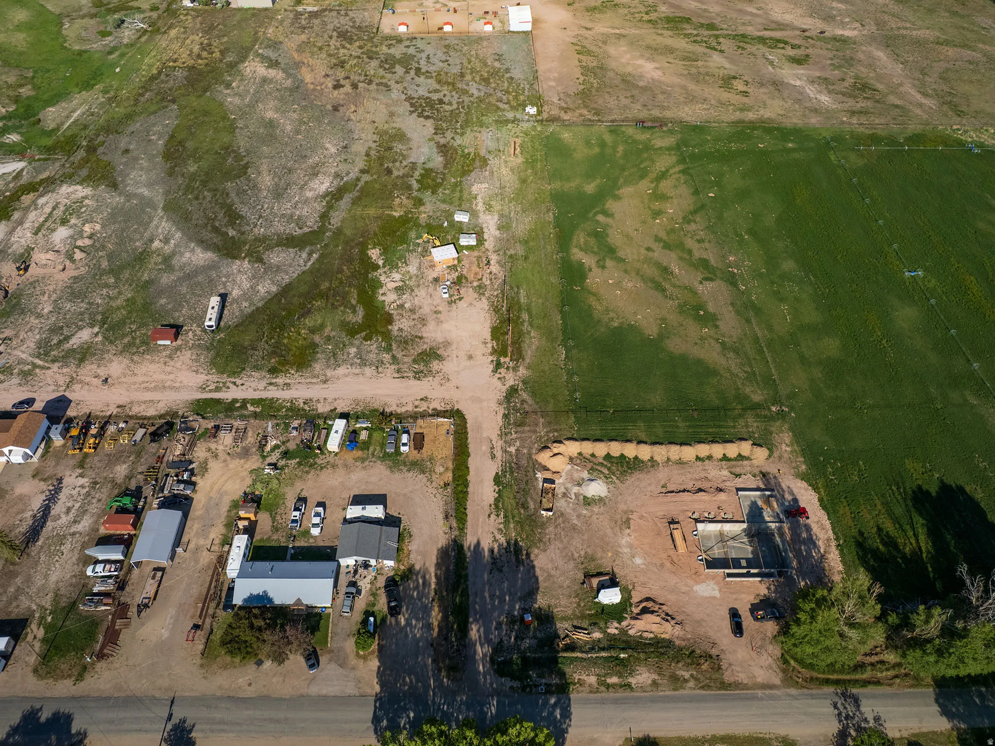 Expansive land parcel featuring a partially constructed structure, a large field of green vegetation, a section of dry vegetation, and a clear road frontage