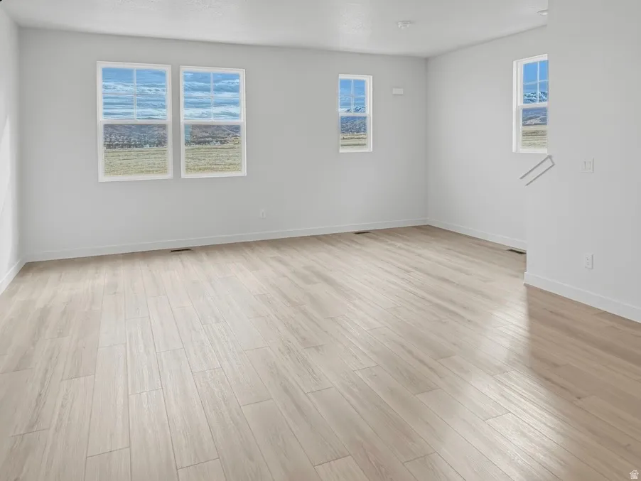 Spacious room featuring light-toned wood-finish flooring and multiple windows