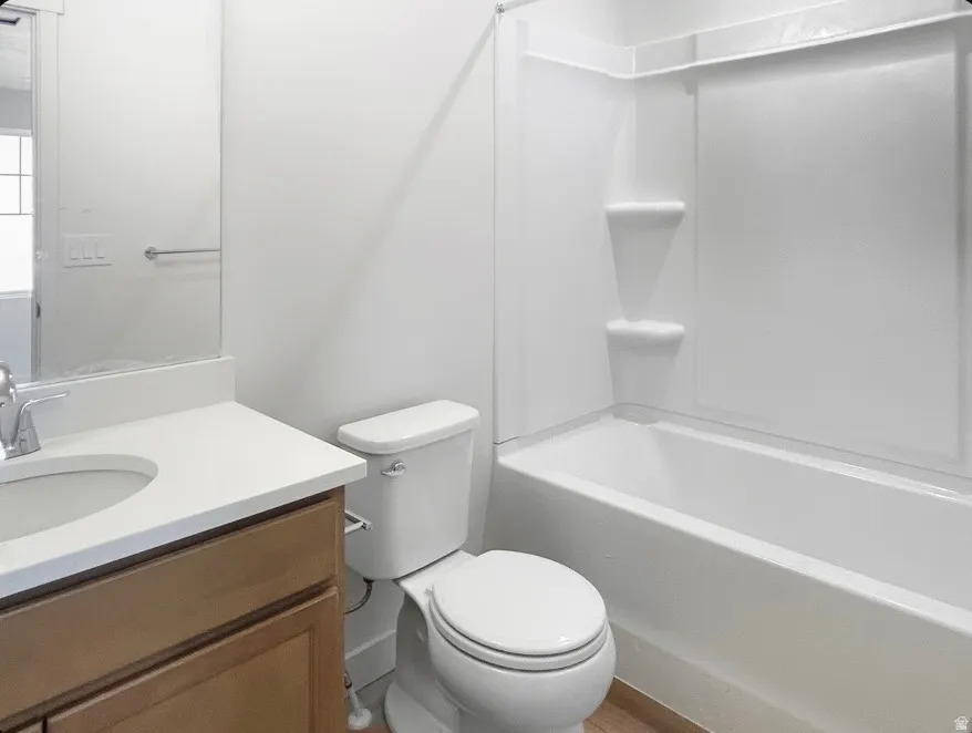 Bathroom featuring a white integrated tub and shower unit, a toilet, and a vanity with a white countertop