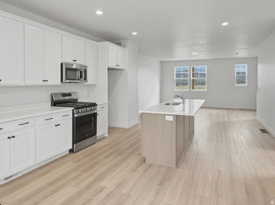 Open-concept kitchen featuring white shaker cabinetry, stainless steel appliances, and a central island with an integrated sink