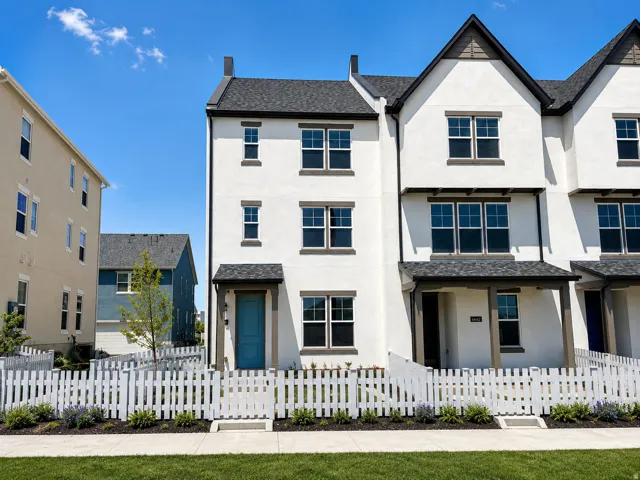 Modern townhome exterior featuring white stucco siding, a charcoal shingle roof, dark trim accents, and a vibrant blue entry door