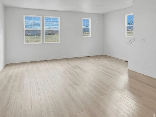 Spacious room featuring light-toned wood-finish flooring and multiple windows