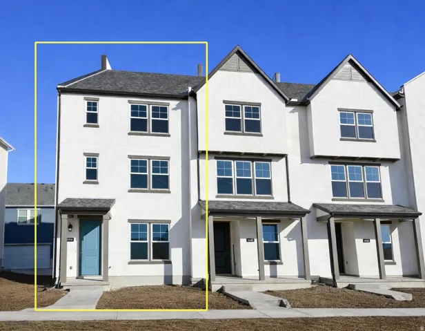 Three-story townhome with a light stucco exterior, dark trim accents, and a blue entry door