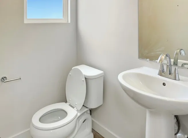 Bathroom featuring a pedestal sink with chrome fixtures, a toilet, a rectangular window, and a wall-mounted mirror