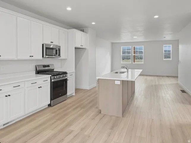Open-concept kitchen featuring white shaker cabinetry, stainless steel appliances, and a central island with an integrated sink