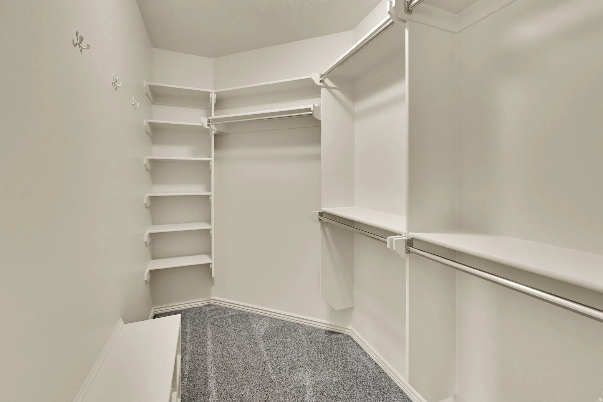 Walk-in closet featuring built-in shelving, multiple hanging rods, and grey carpeting