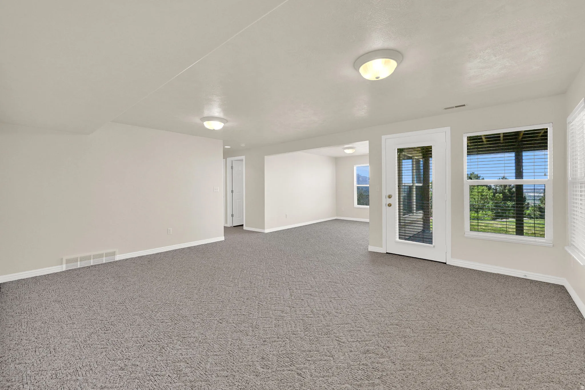 Spacious room with grey patterned carpeting, light neutral wall paint, and white trim