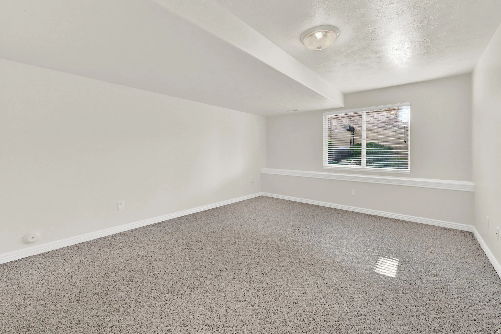 Carpeted interior space featuring neutral wall tones, a recessed window with horizontal blinds, overhead flush mount lighting, and a partial decorative chair rail