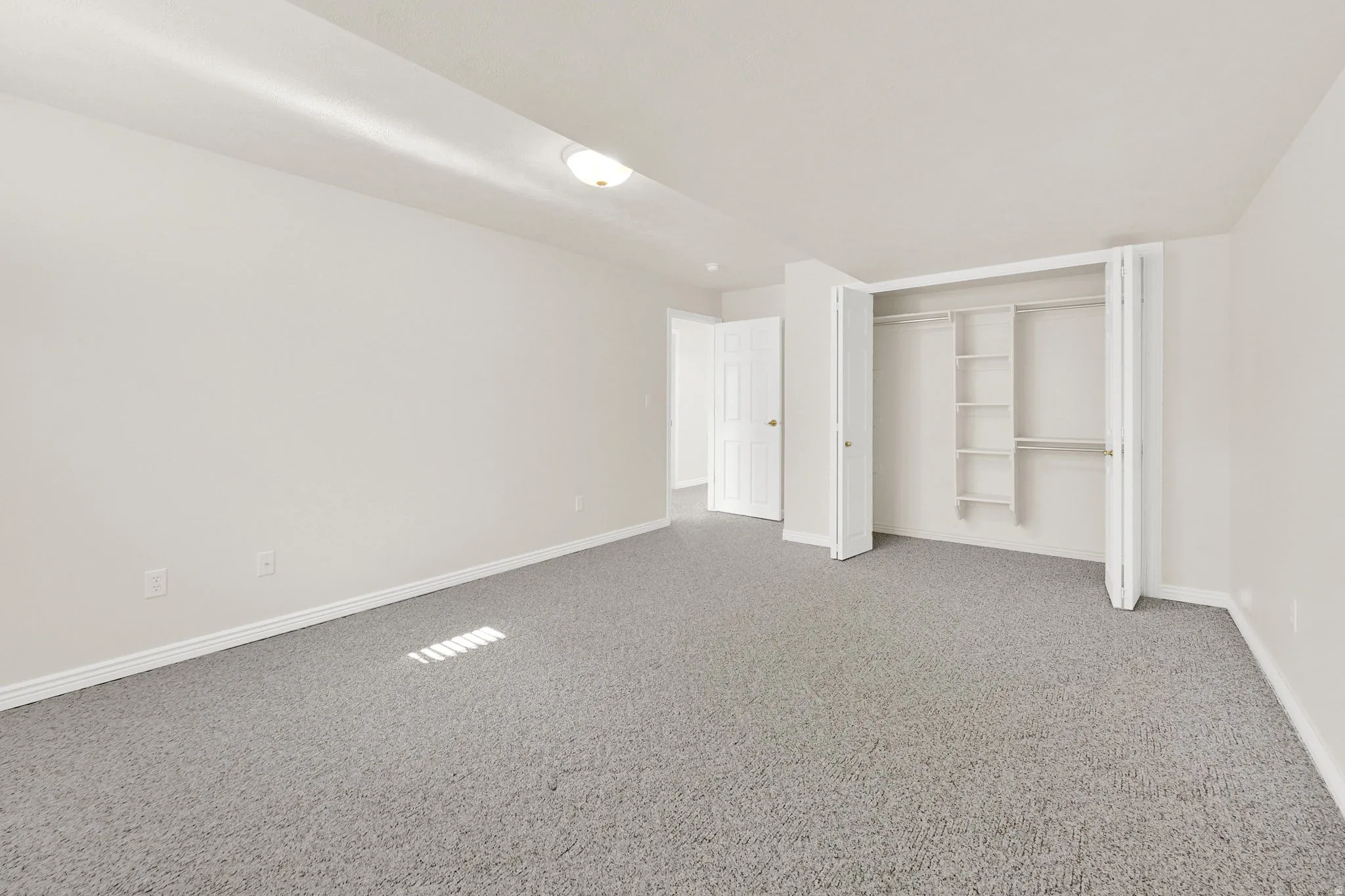 Spacious room featuring light gray carpeting, white walls, white baseboards, and a built-in closet with shelving and hanging rods