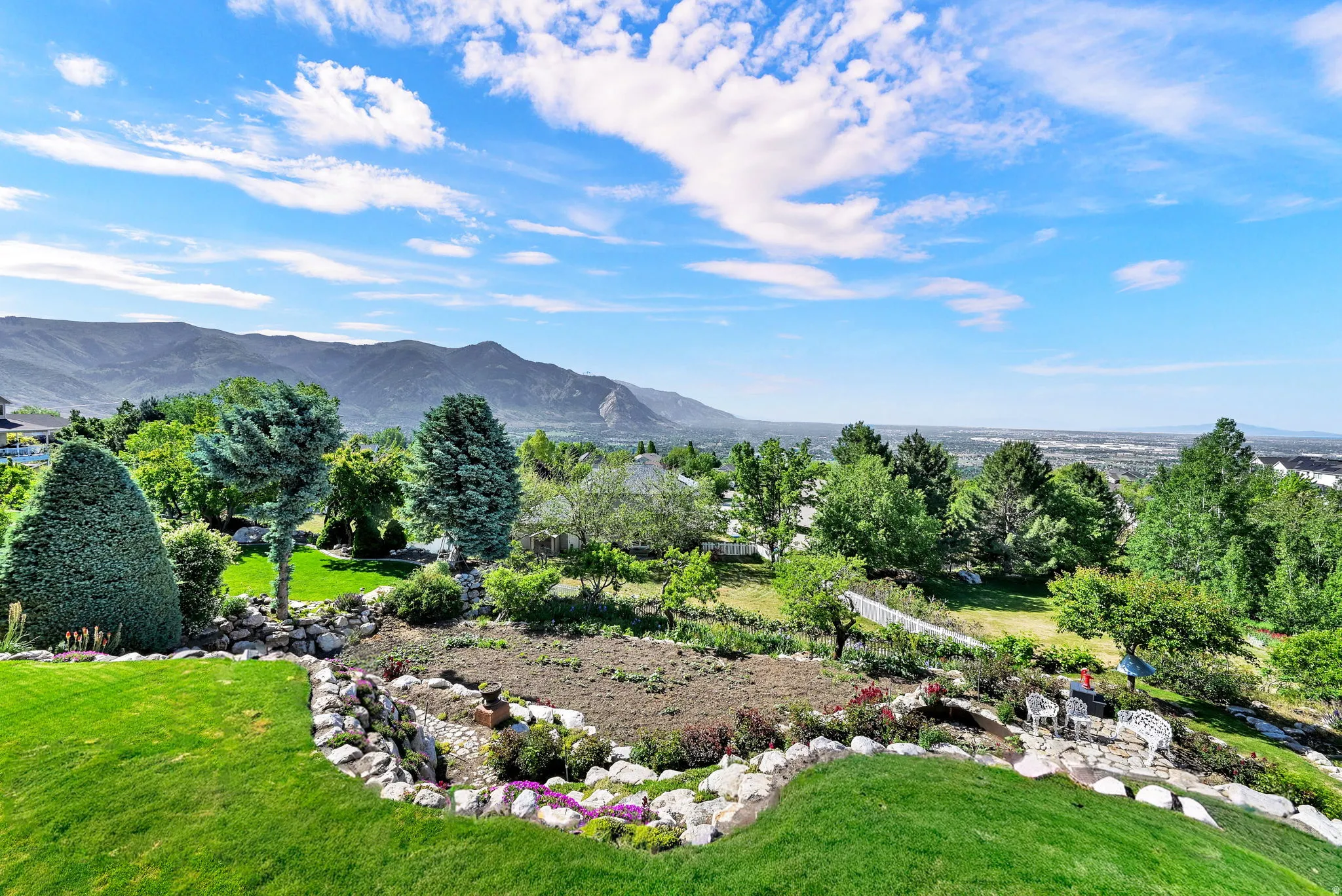 Expansive hillside property featuring a tiered yard with manicured lawns, mature trees, and landscaping elements
