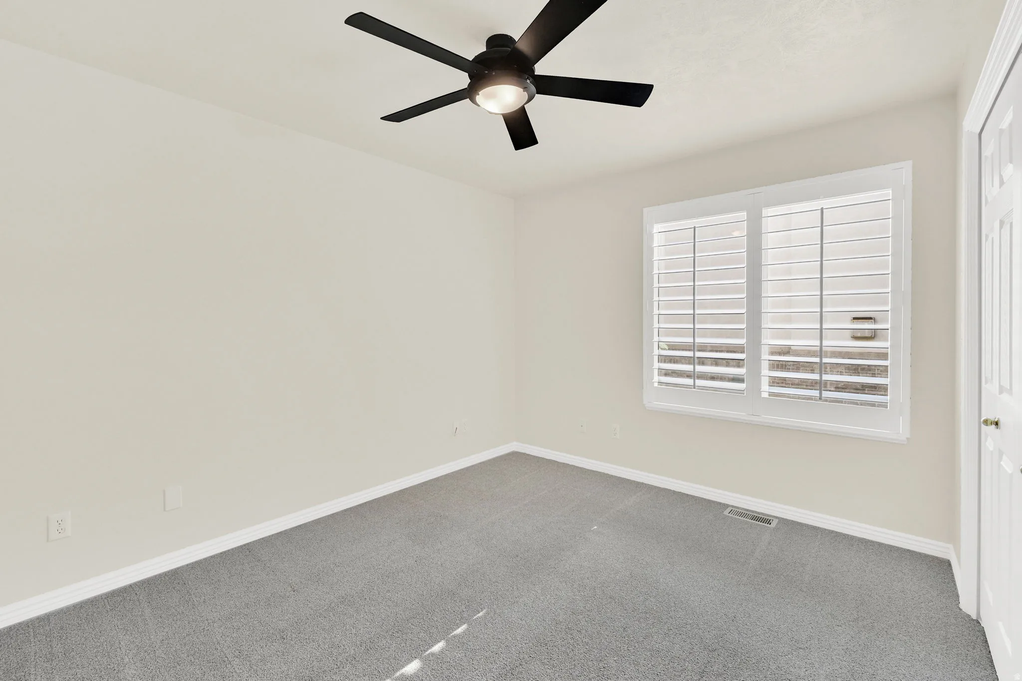 Light-filled room featuring a ceiling fan with light fixture, neutral carpeting, and a window with plantation shutters
