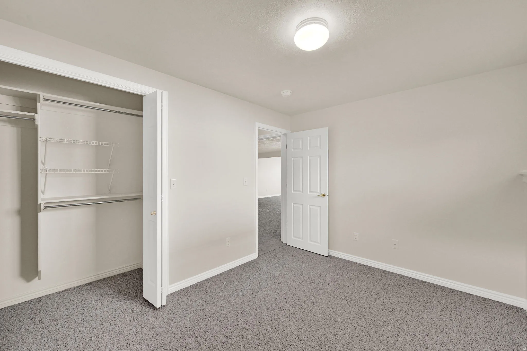 Bedroom featuring neutral wall paint, gray carpeting, a built-in closet with wire shelving and hanging rods, a white paneled door, and an overhead flush-mount light fixture