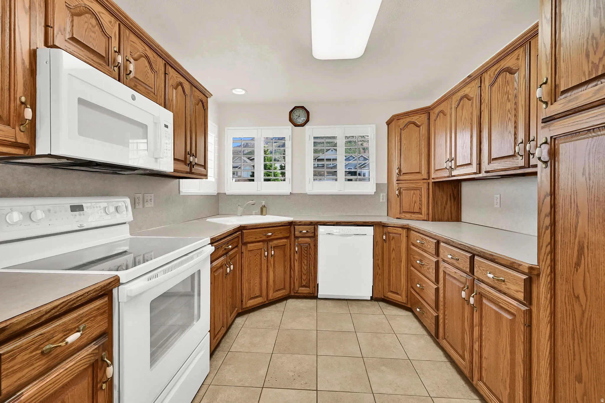 U-shaped kitchen featuring wood cabinetry, white appliances, and tiled flooring