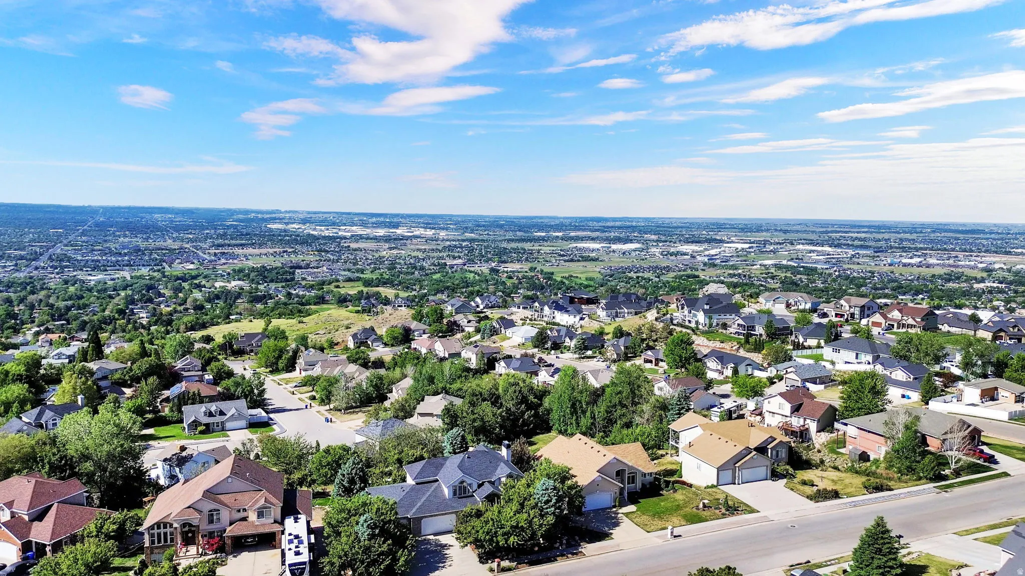 Expansive residential area featuring numerous single-family homes, mature tree coverage, and clear blue skies