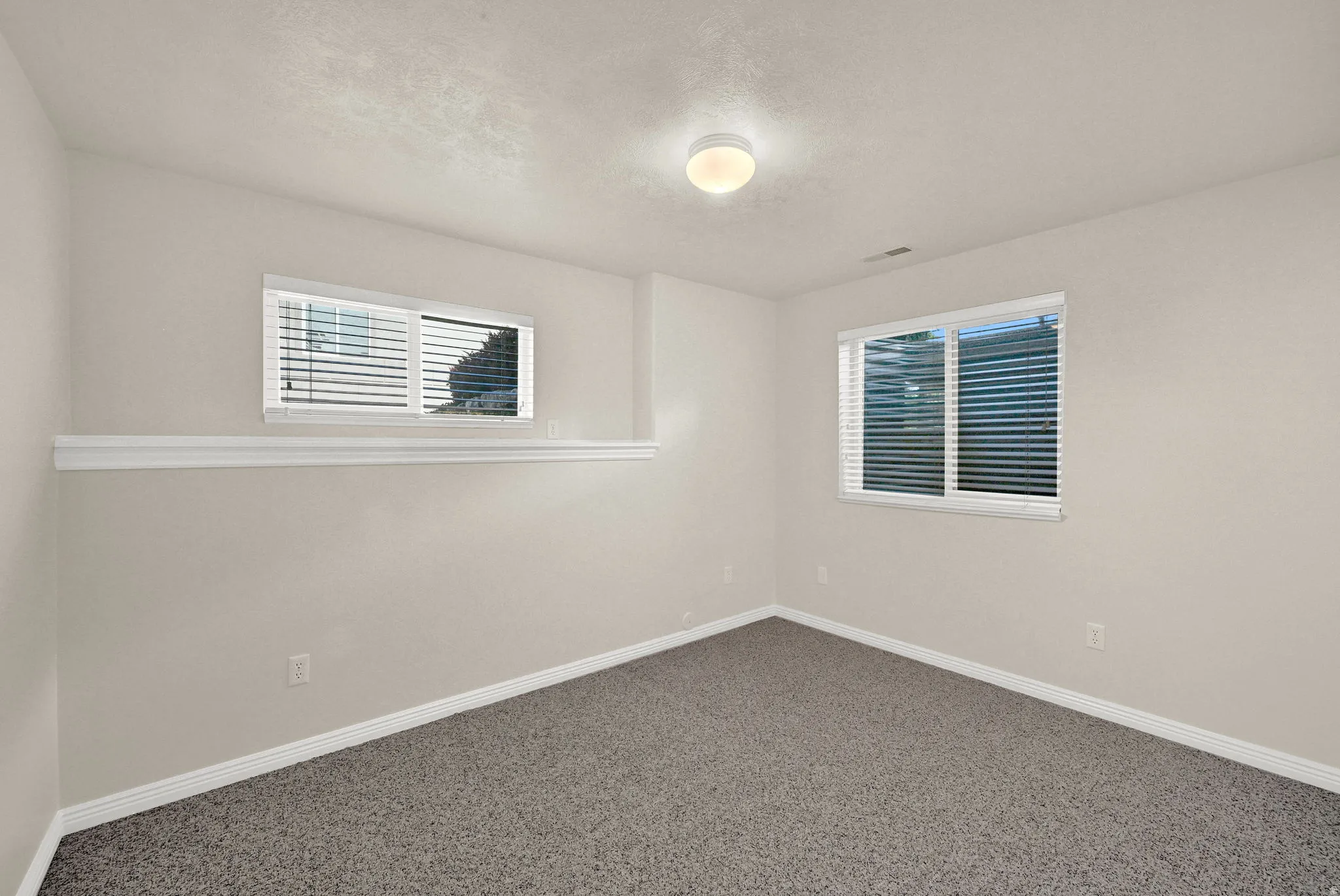 Spacious room featuring neutral paint, gray textured carpet, and white baseboards