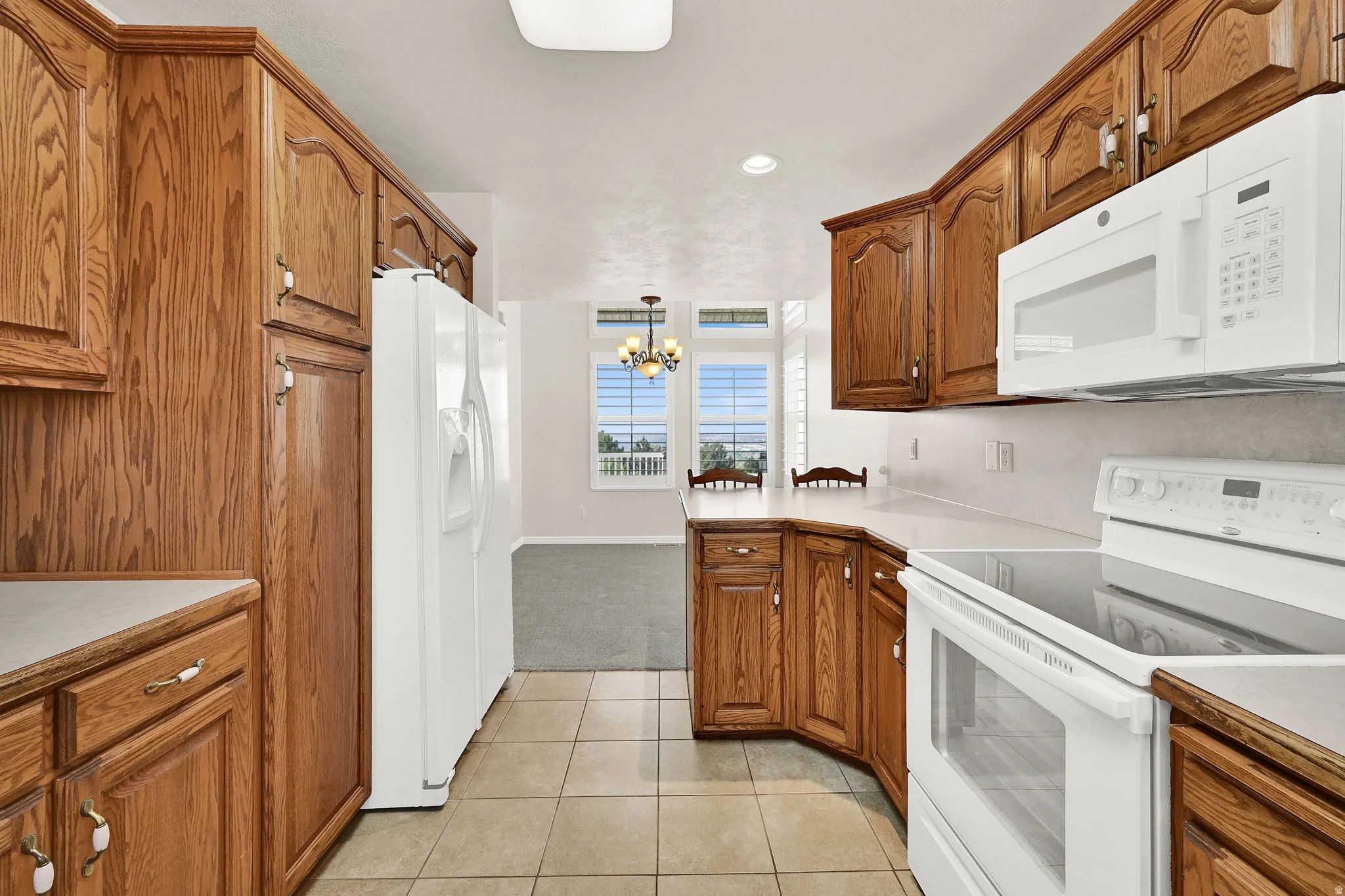 Kitchen featuring wood cabinetry, white appliances, light-toned countertops, and tile flooring