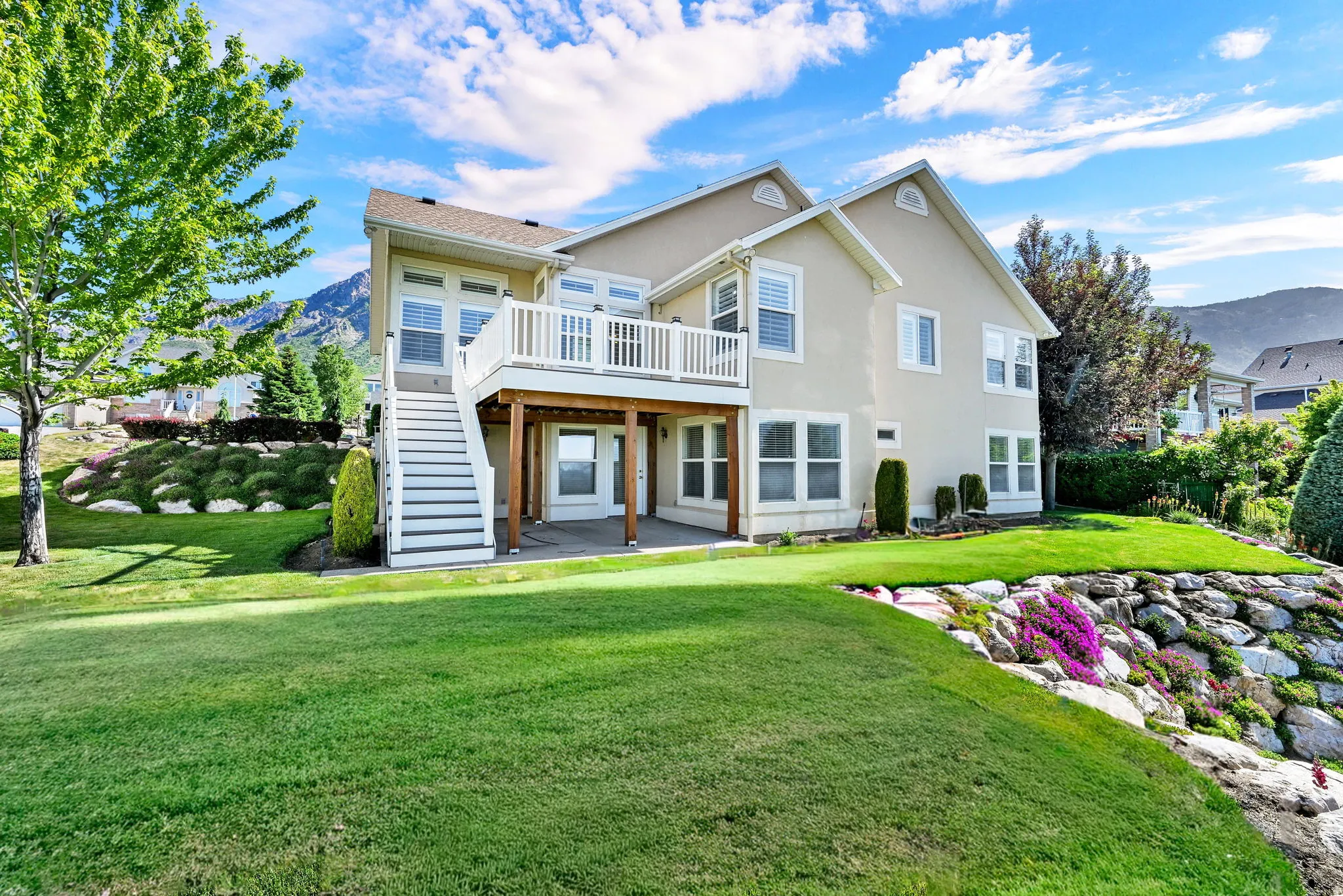 Rear exterior featuring a two-story stucco facade, second-story balcony with white railing, covered patio, and a staircase descending to the lawn