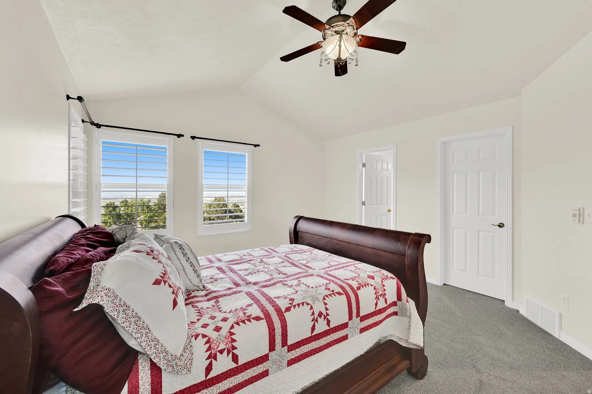 Vaulted ceiling room featuring a decorative ceiling fan with integrated lighting, two windows with white plantation shutters, and light-colored carpeting