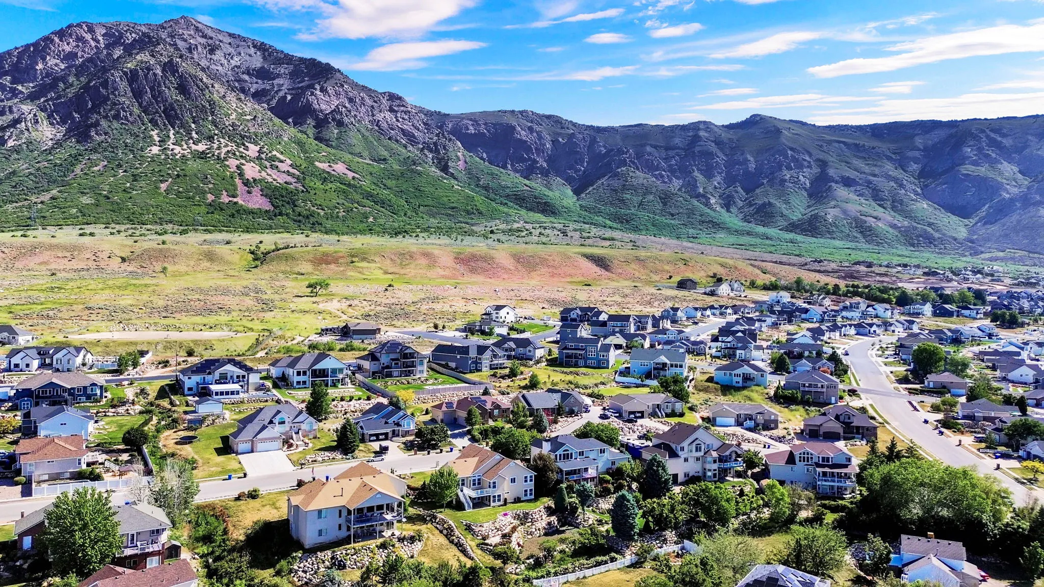 Expansive residential development featuring varied architectural styles and asphalt streets, set against a backdrop of prominent mountains and natural terrain
