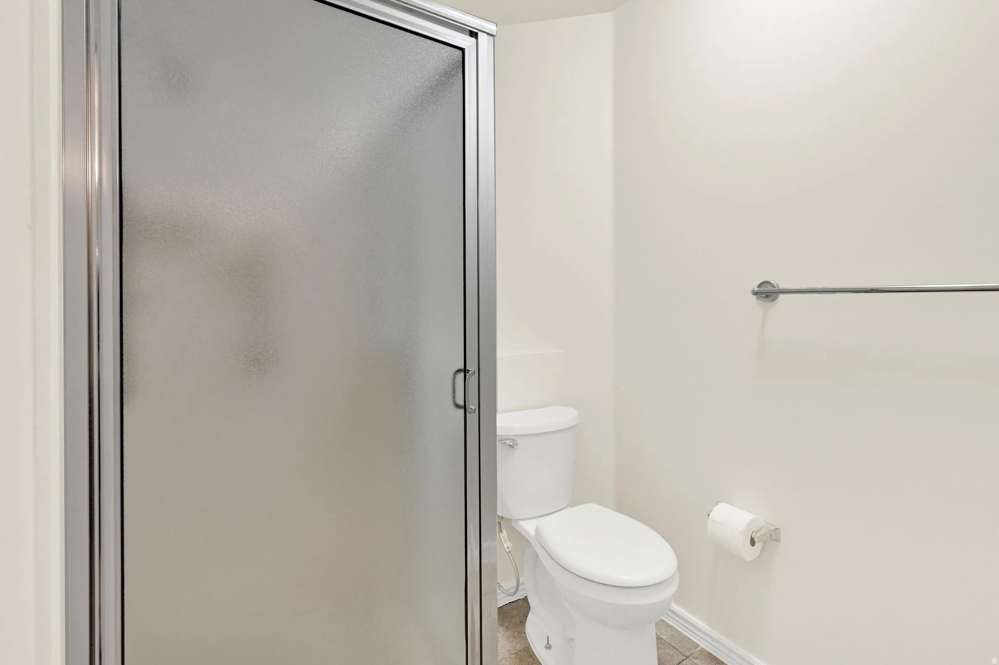 Frosted glass shower enclosure with chrome framing, white toilet, and tile flooring